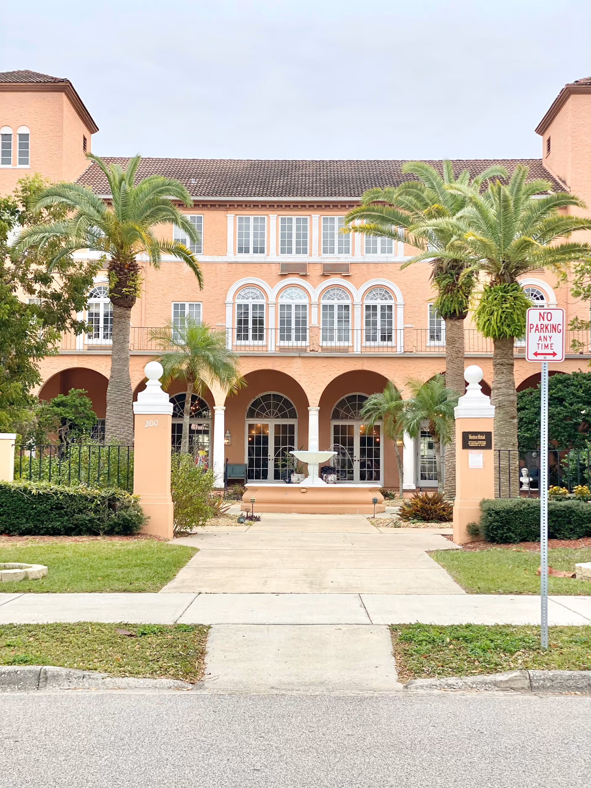 Pink stucco senior living facility front with arches, palm trees, and a fountain.