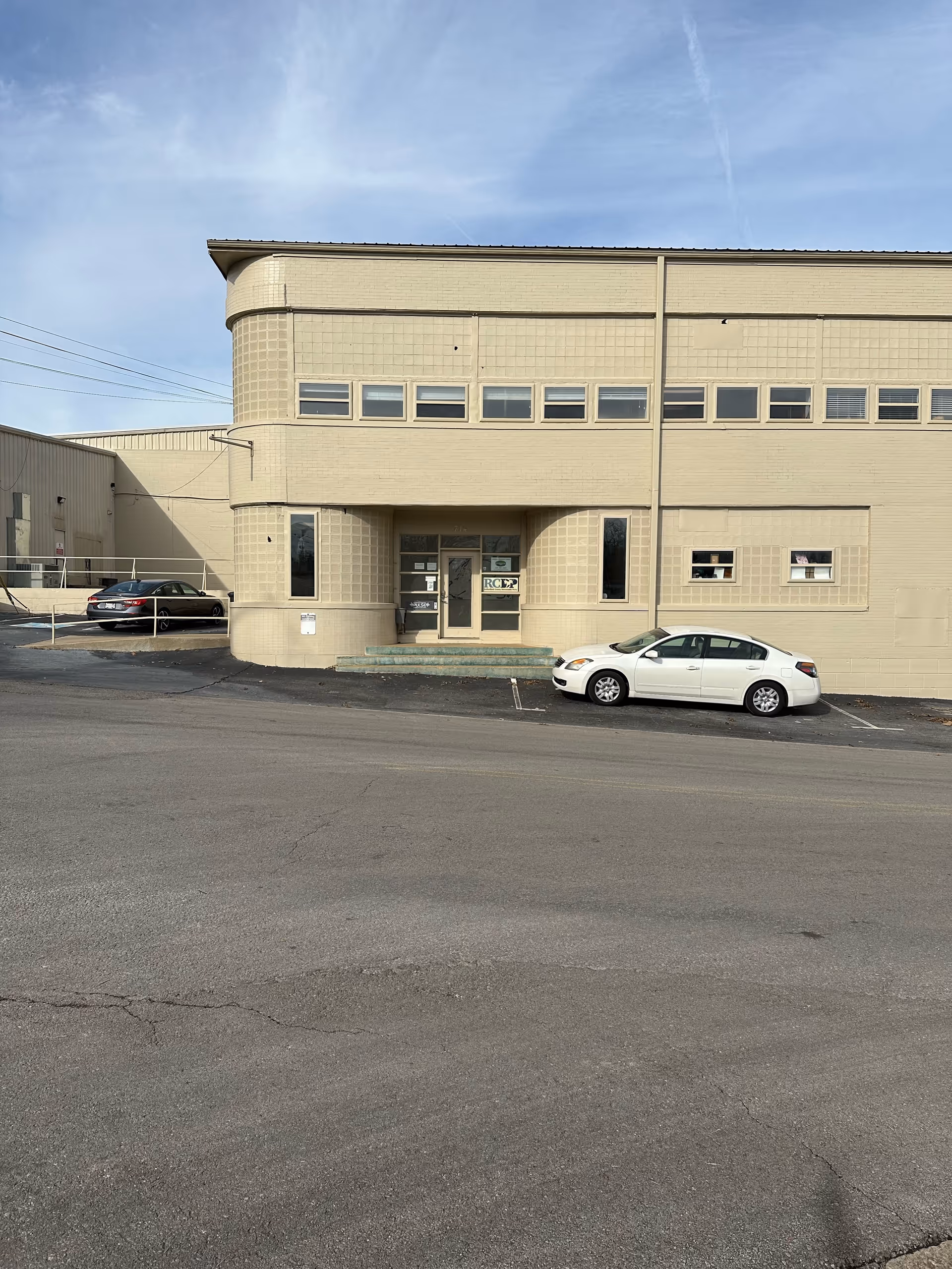 Beige two-story building entrance with parked cars and a blue sky.