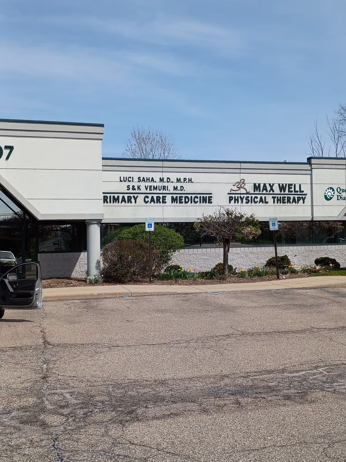 Front view of a medical clinic building with signs and a parking lot.