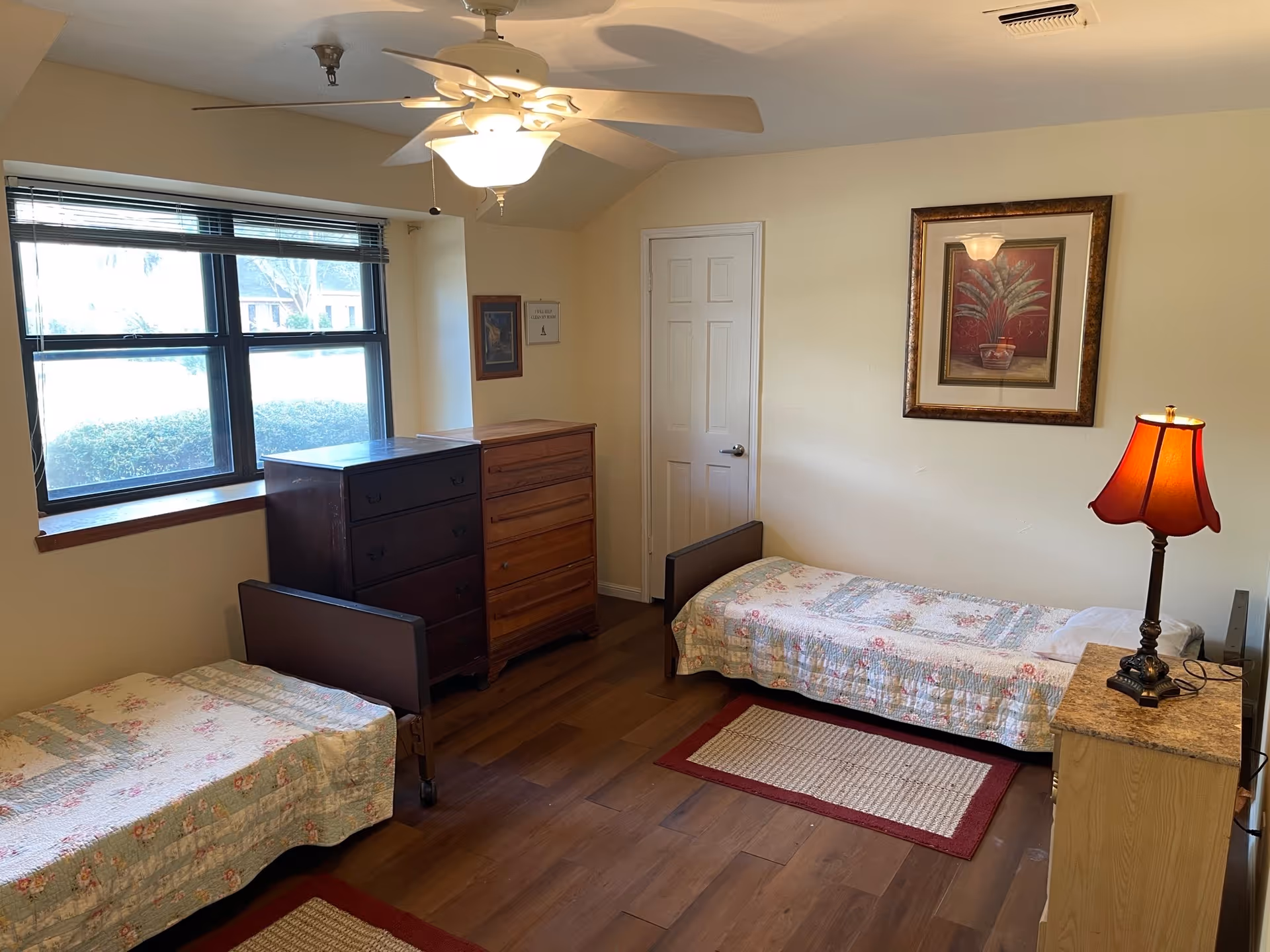 Two single beds with quilts, dressers, a window, and framed wall art.
