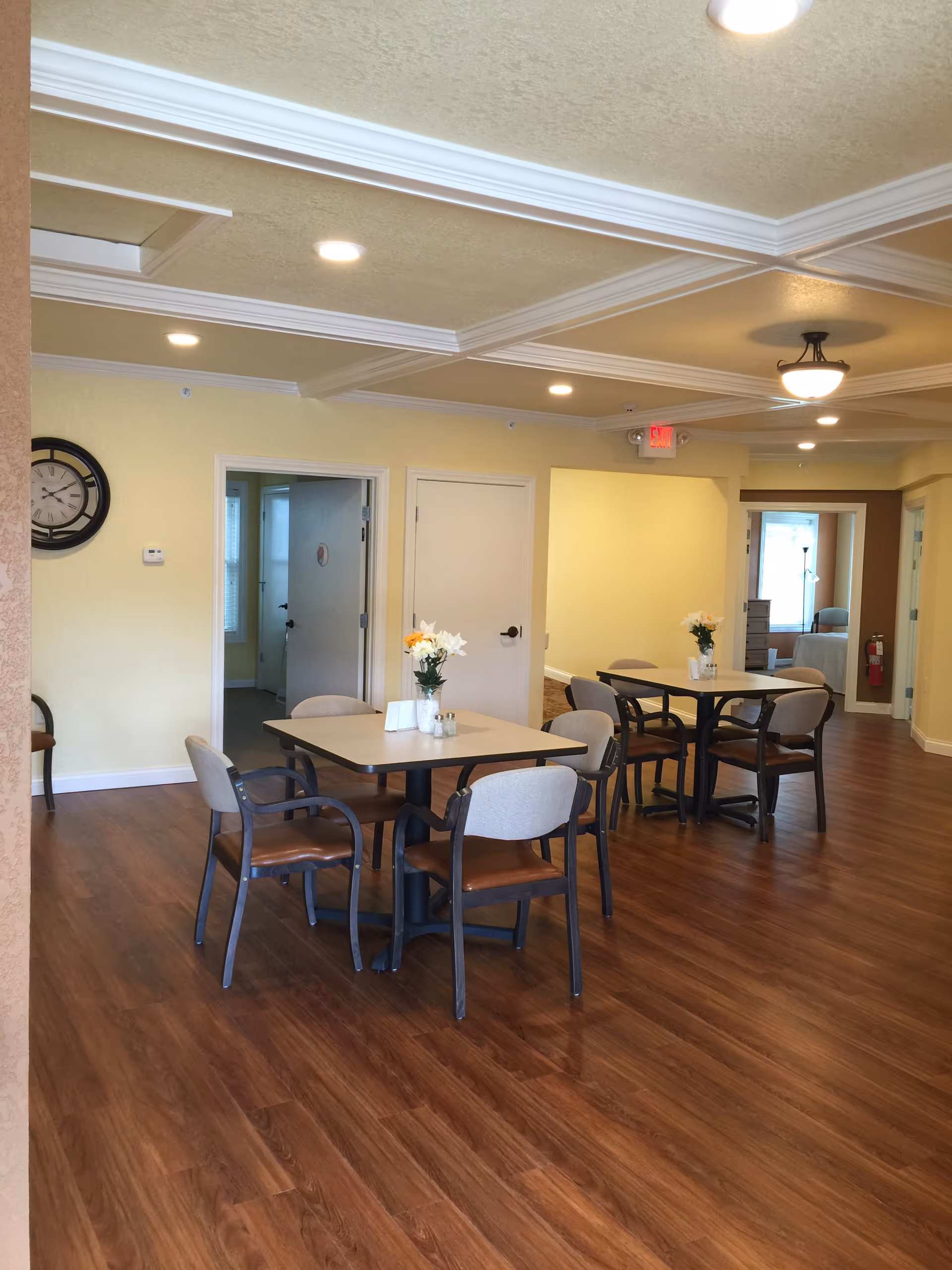 Bright dining area in a senior living facility with tables, chairs, and flowers.