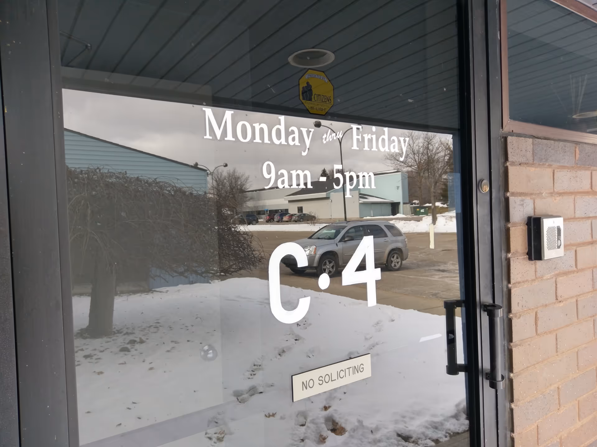 Glass front door showing hours, snow outside, and building entrance.