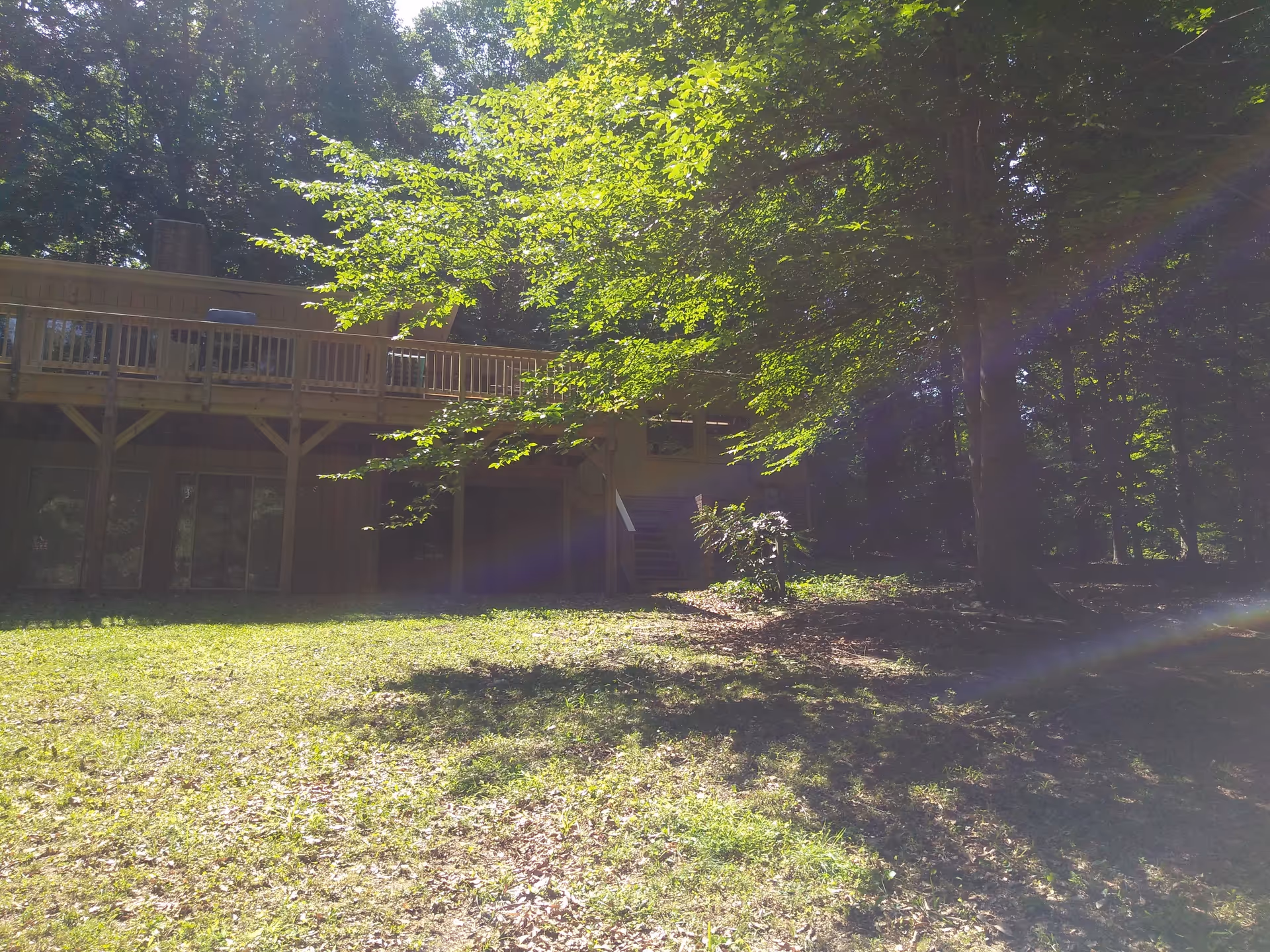 Wooden two-story building with an elevated deck surrounded by trees and grassy yard.