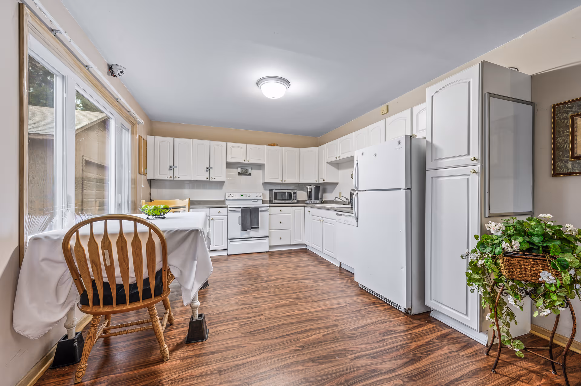 Bright white kitchen with cabinets, appliances, and a table by the window.