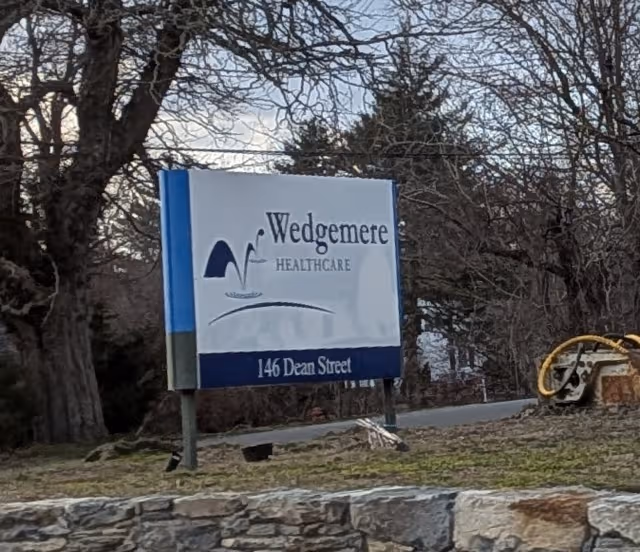 Outdoor sign reads Wedgemere Healthcare, address 146 Dean Street, set among trees.