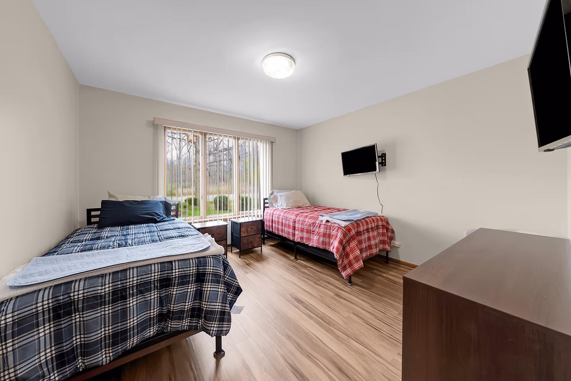 Bright shared bedroom with two twin beds, plaid duvets, and a window view.