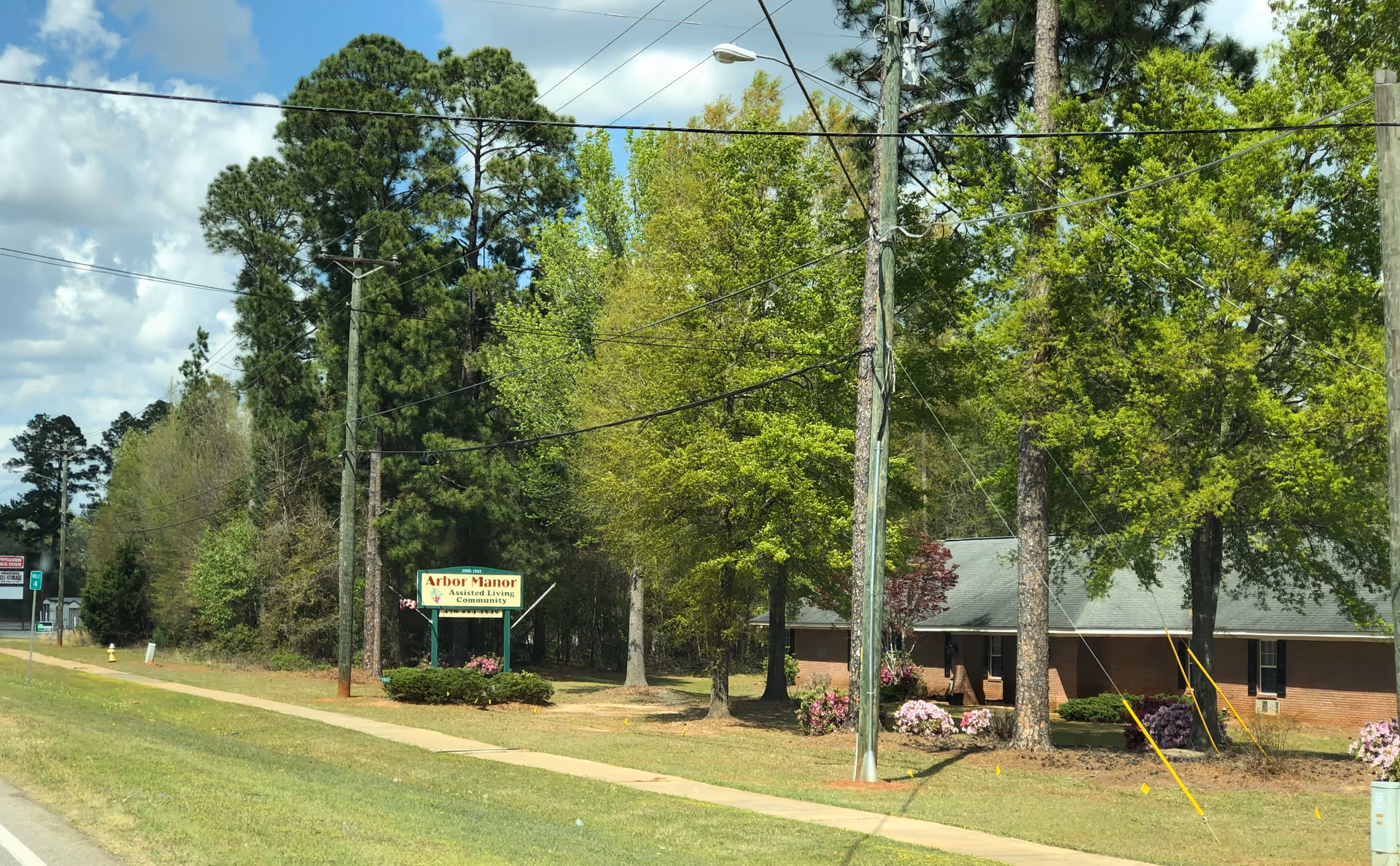 Brick Arbor Manor building front with sign, trees, and a sidewalk along the road.