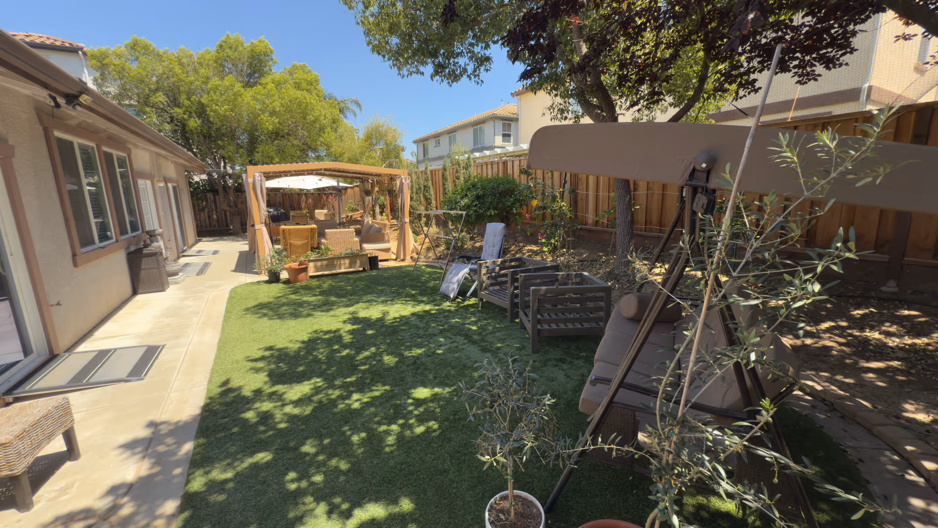 Sunny backyard with patio seating, lounge chairs, pergola, and potted plants.
