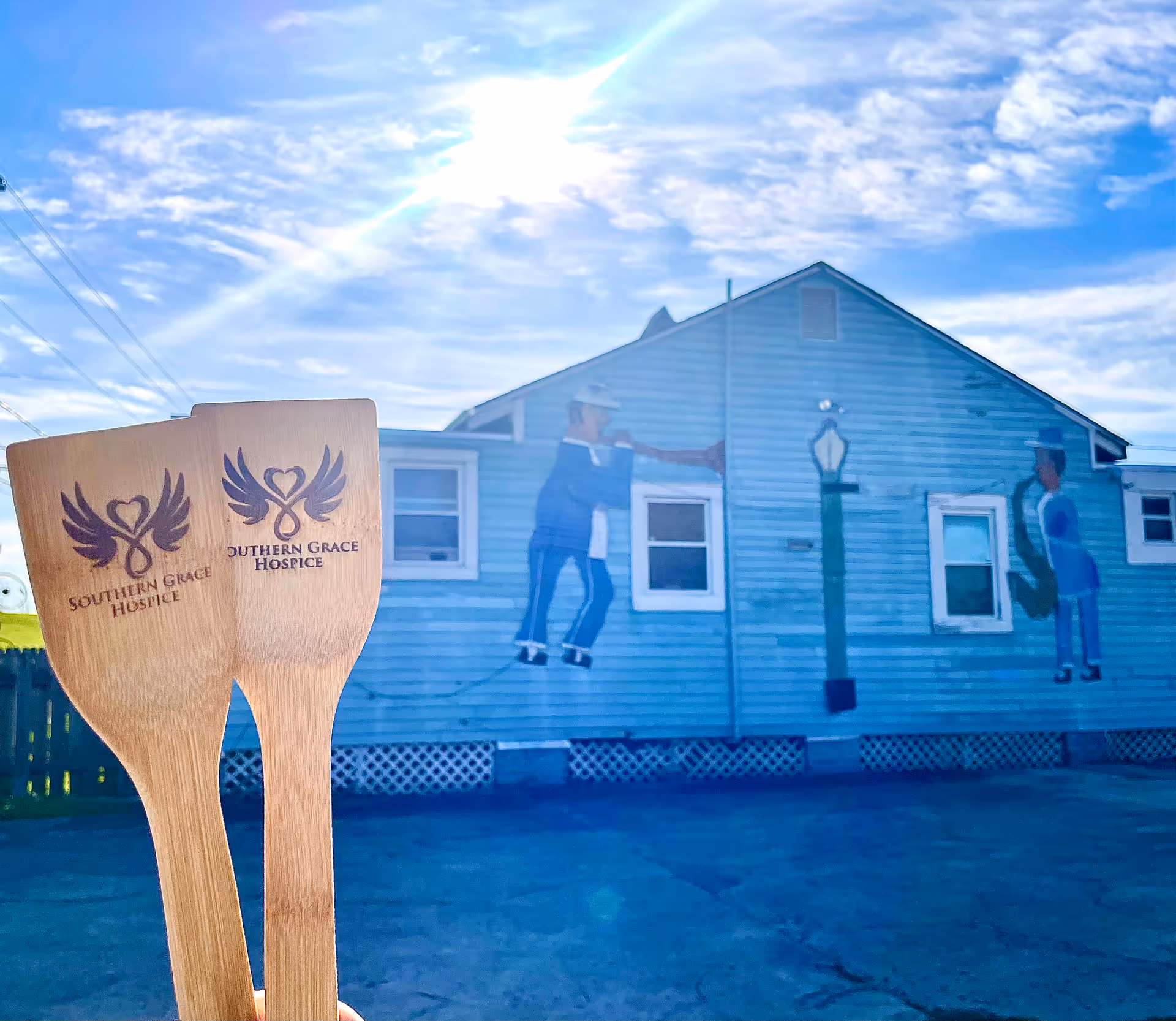 Blue building exterior with mural figures and two wooden spoons branded Southern Grace Hospice in foreground