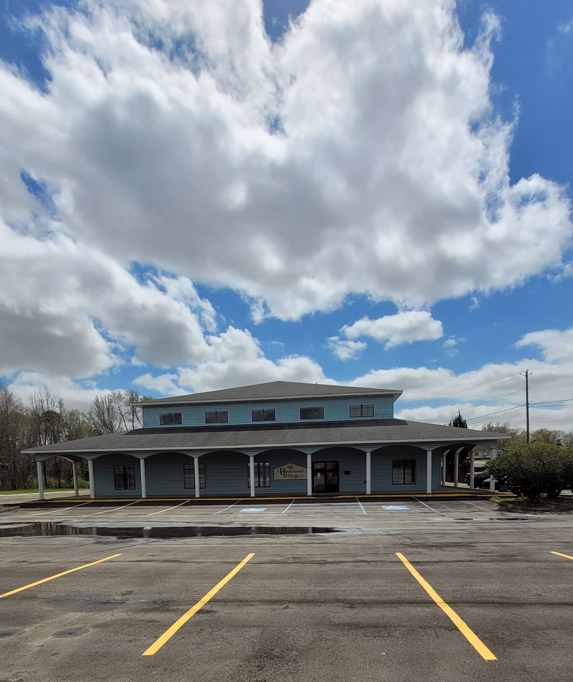 Blue two-story building housing Traditions Health Hospice, with a wide covered porch and empty parking lot.