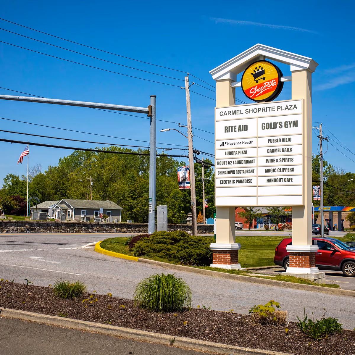 Bright outdoor scene of a Carmel ShopRite Plaza sign listing stores against a blue sky.