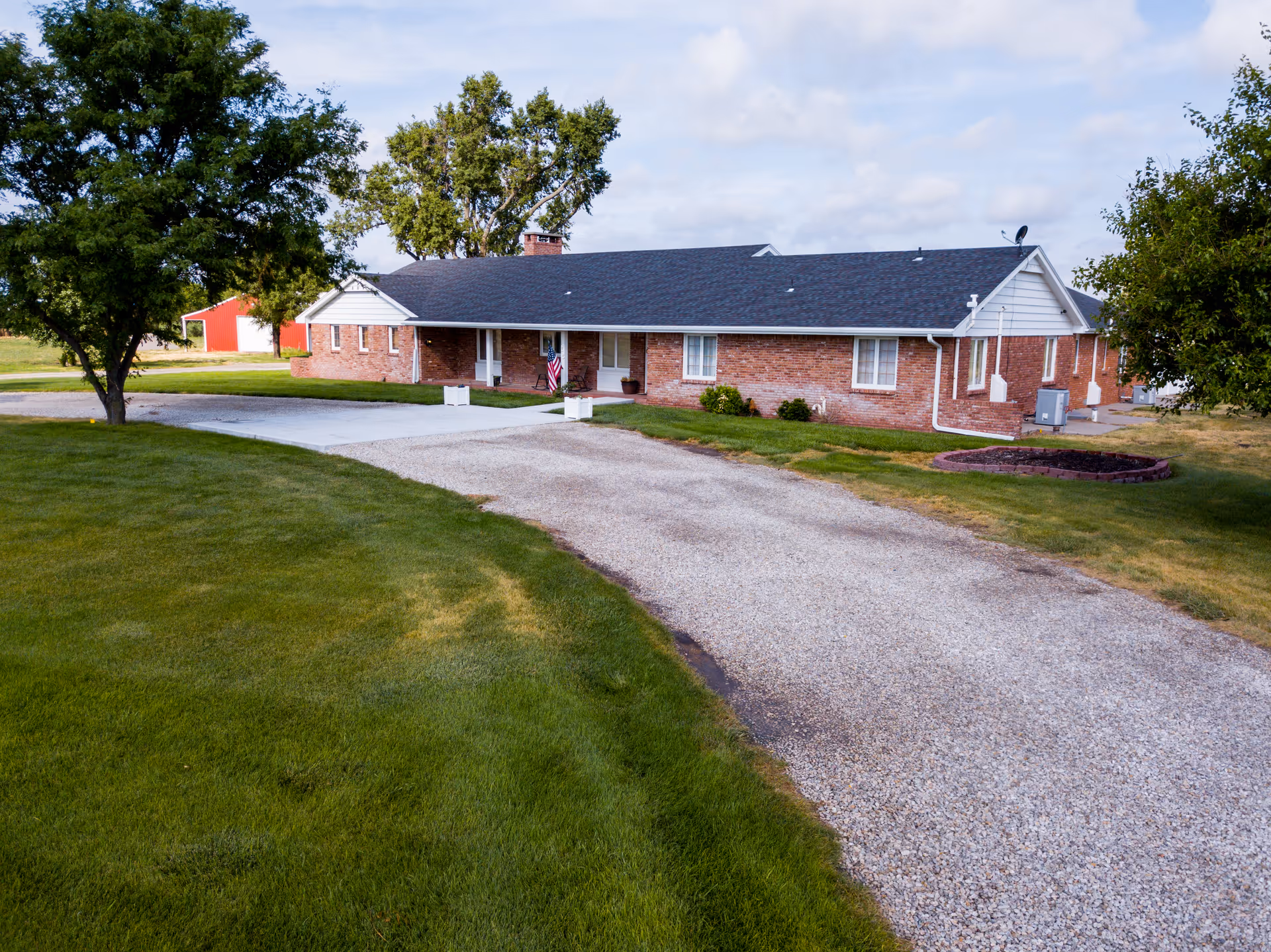 Aster Estates senior living facility exterior with brick walls, gravel driveway, and green lawn.