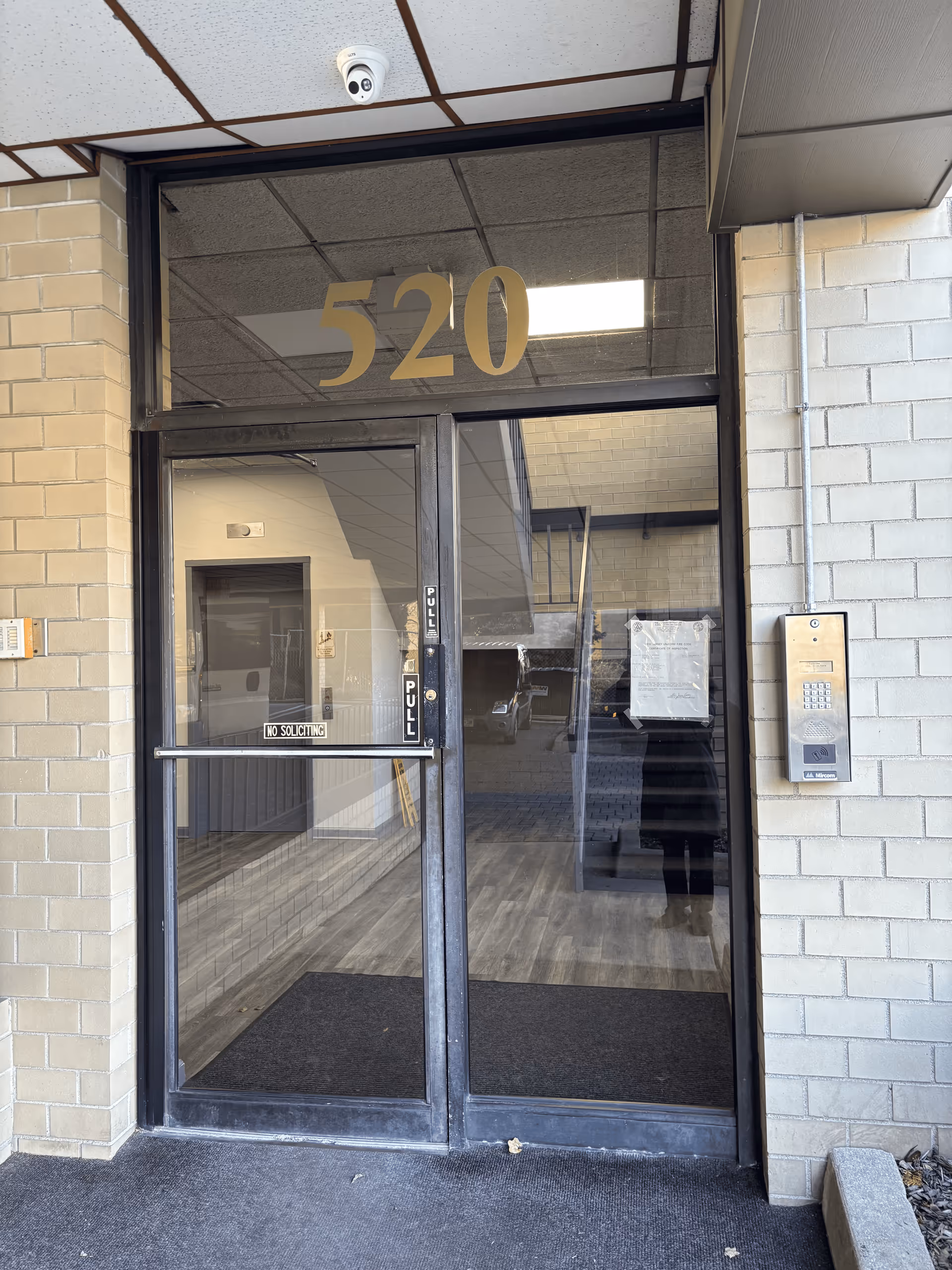 Glass entrance with the number 520 and security camera on a brick facade.