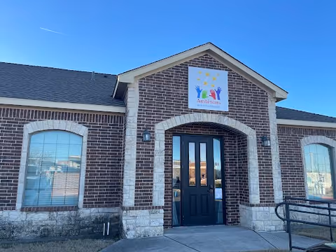 Brick facility exterior featuring arched doorway, large windows, and Ambitions sign above entrance.