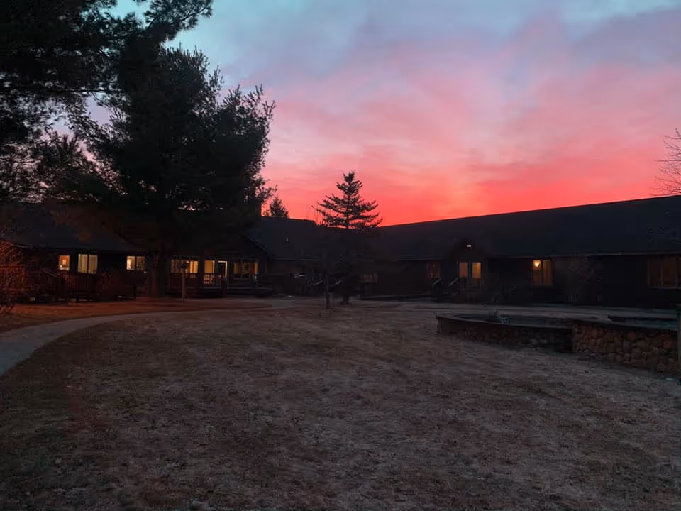 Single-story senior living building and courtyard under a vivid pink sunset with illuminated windows.