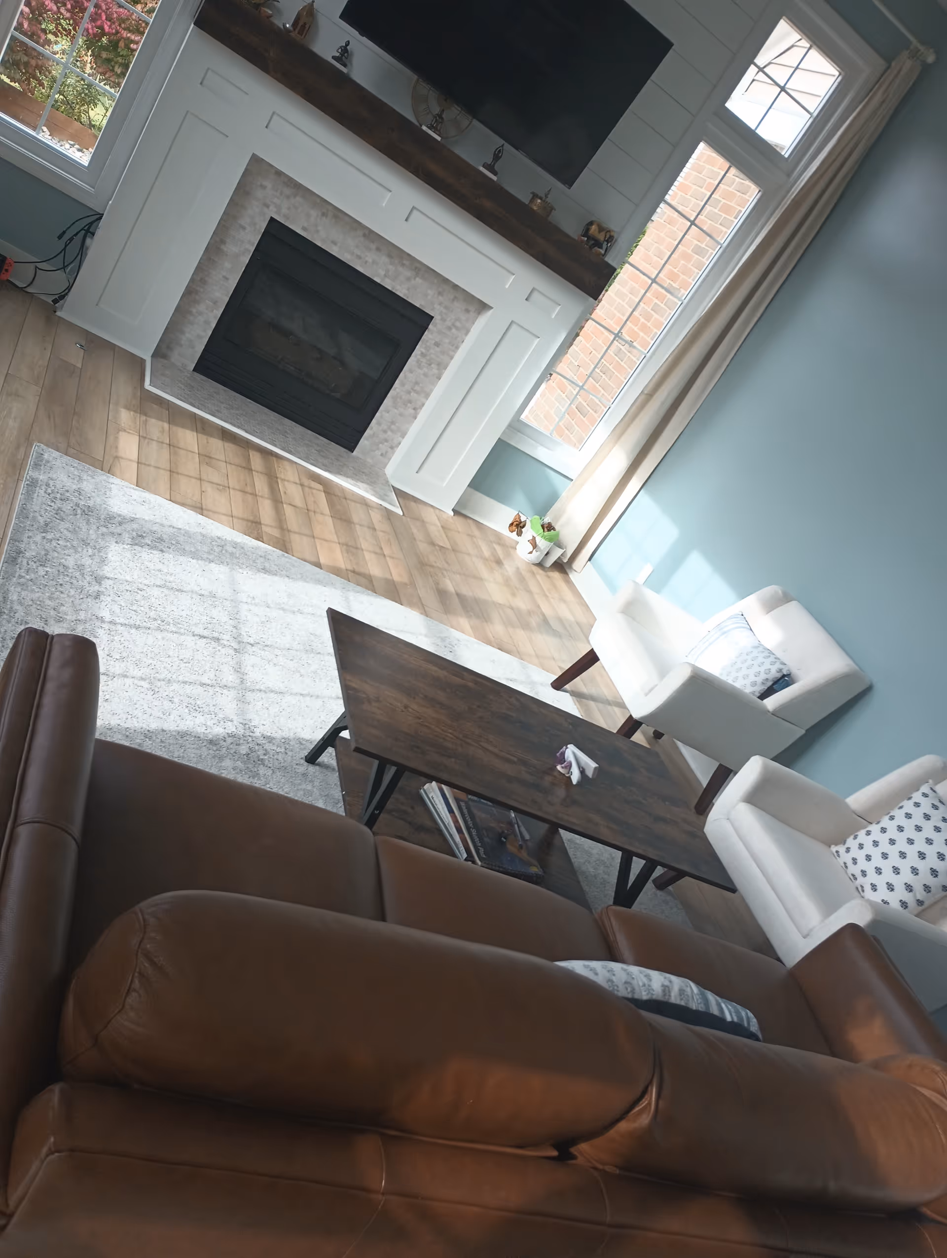 Living room with brown leather sofa, fireplace, TV, and bright windows.