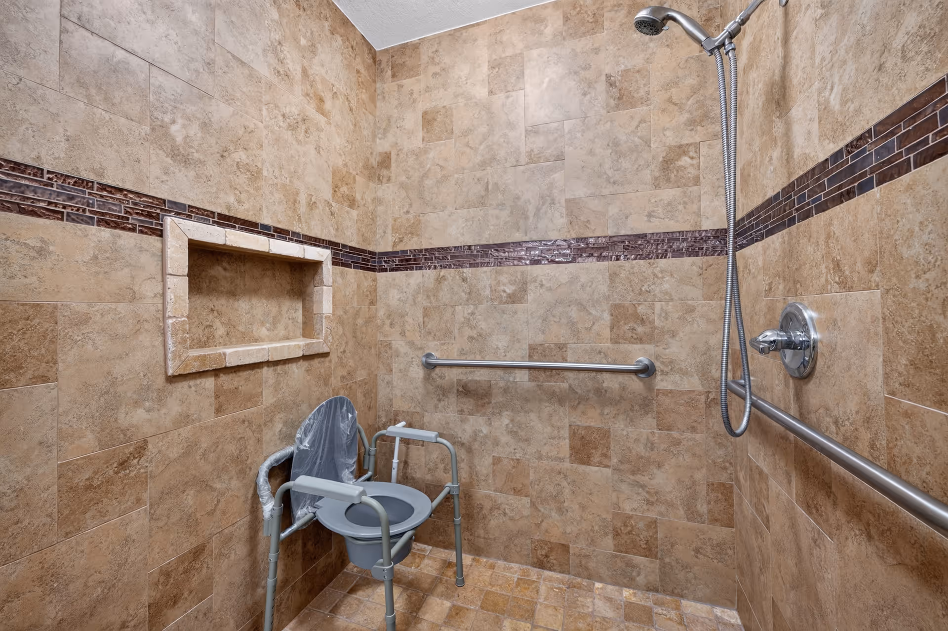 Accessible bathroom with tiled walls, shower head, grab bars, and a shower chair.