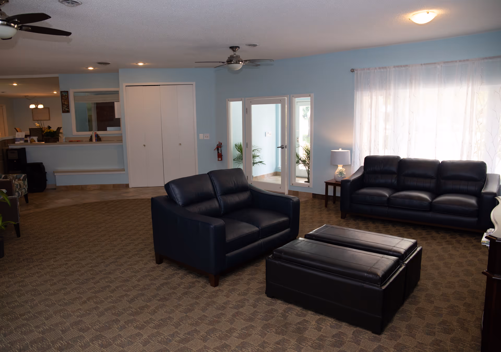 Spacious senior living lounge with blue walls, two dark leather couches, and a reception area.