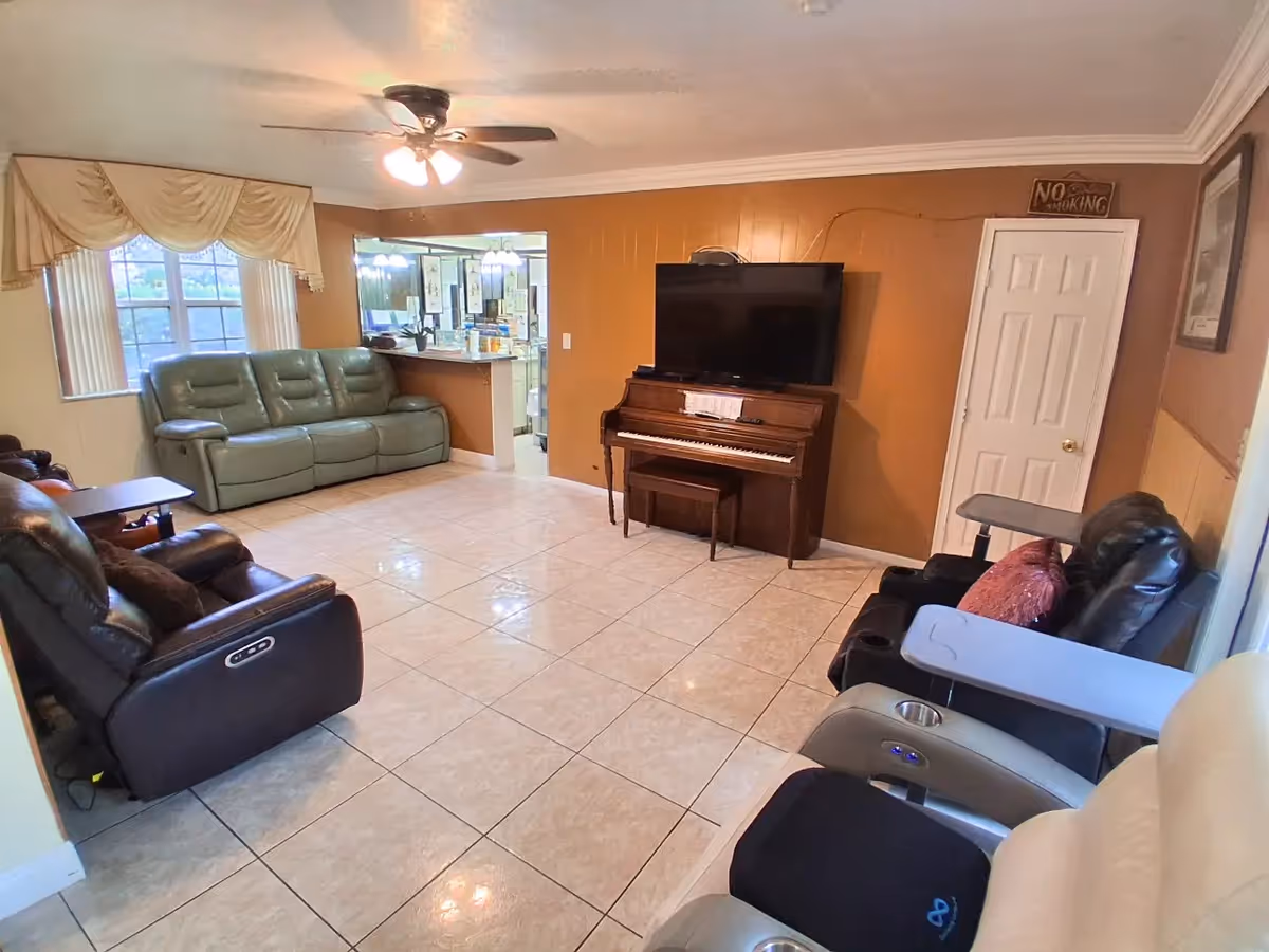 Cozy common living room with a piano, TV, and several reclining chairs.