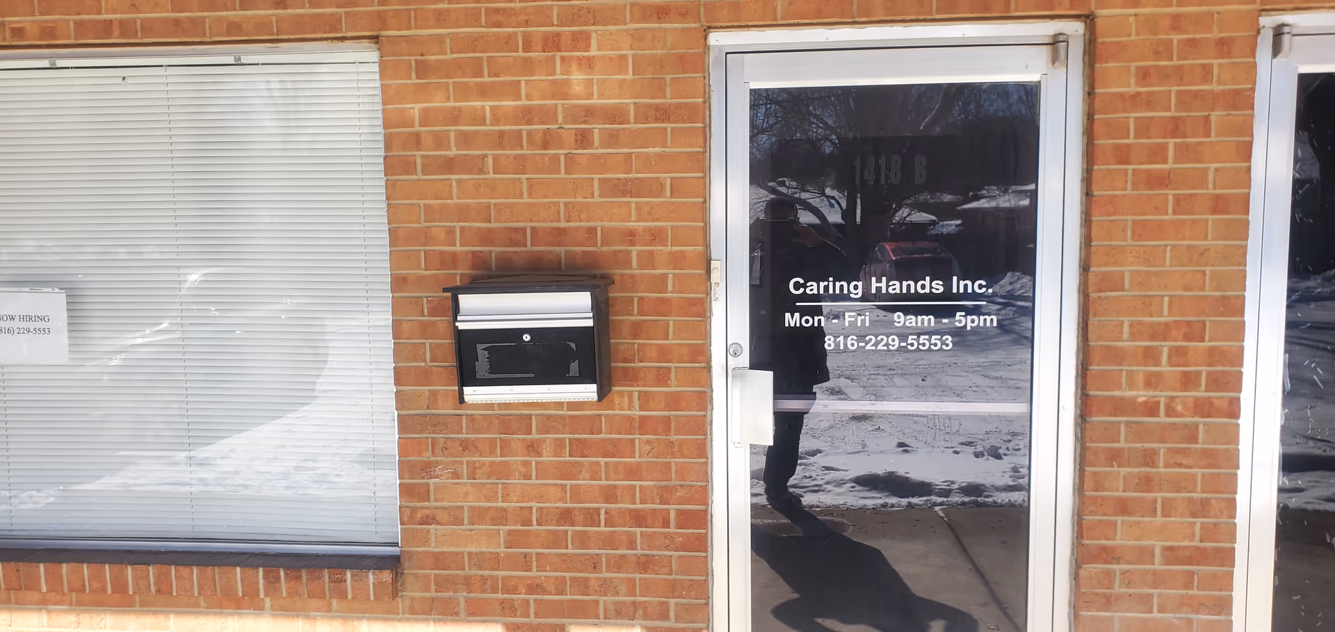 Brick building exterior with glass door displaying Caring Hands Inc. entry and hours.