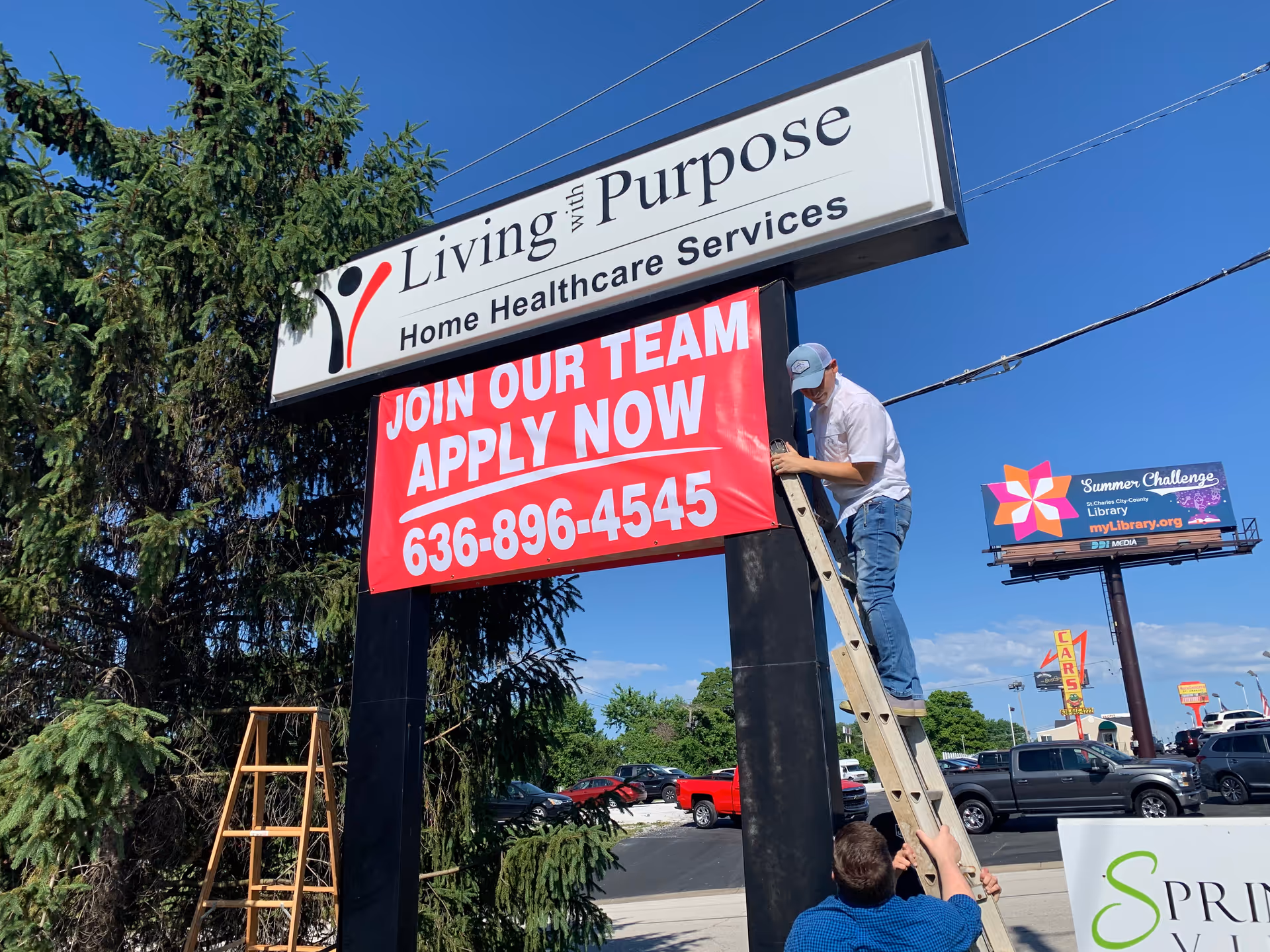 A man on a ladder adjusts a sign for Living with Purpose Home Healthcare Services outdoors.