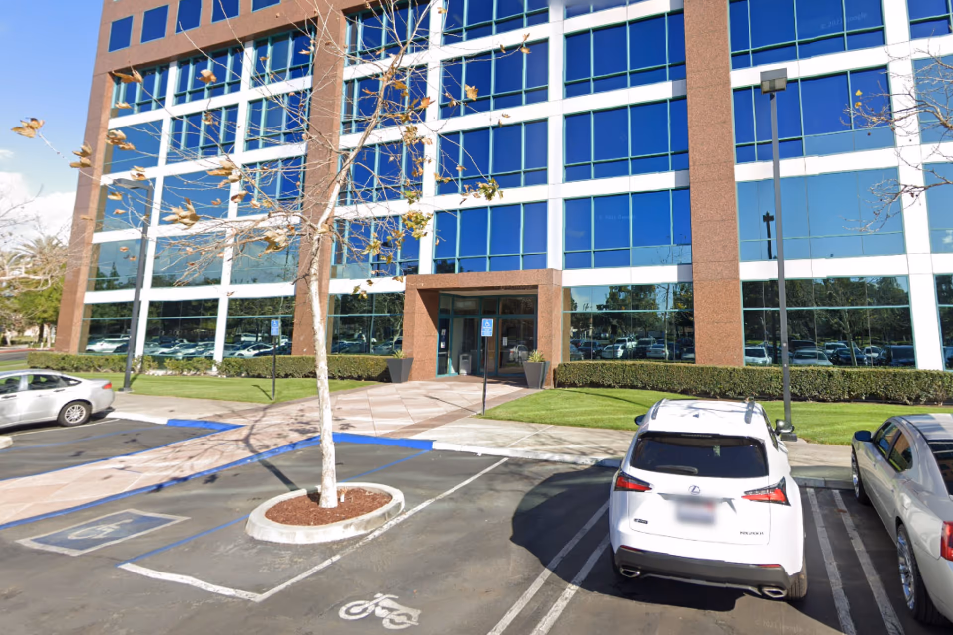 Glass-front office building with a parking lot and leafless trees.