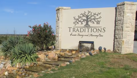 Outdoor entrance sign for Traditions Senior Living and Memory Care with plants and rocks.