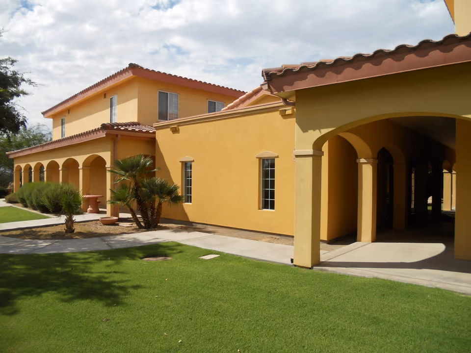 Yellow stucco senior living building with arches and palm trees in front lawn.
