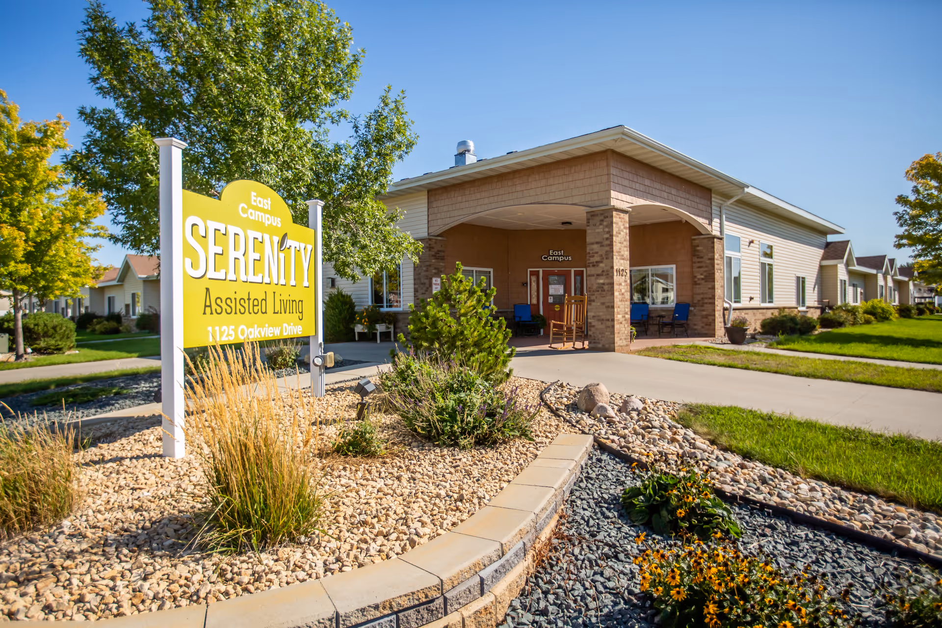 Exterior view of Serenity Assisted Living facility with sign, entrance porch, and landscaped grounds.
