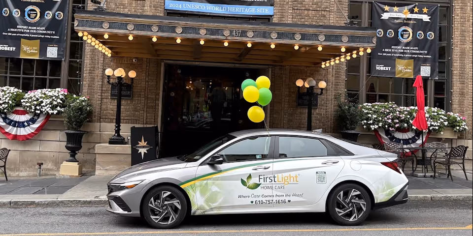 A FirstLight Home Care vehicle parked in front of a stone building entrance with balloons.