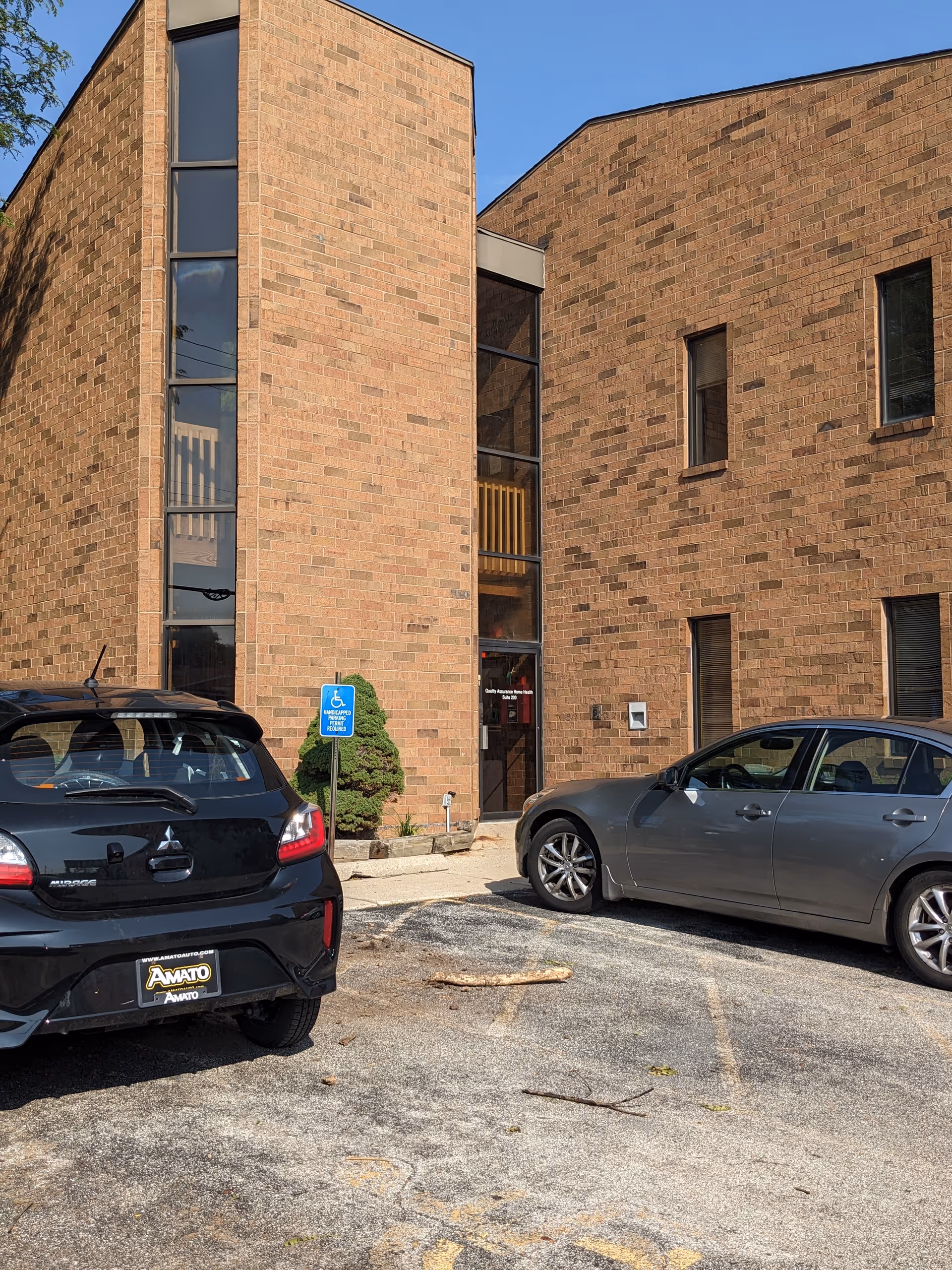 Brick building facade with tall windows, wheelchair sign, and parked cars at the entrance.