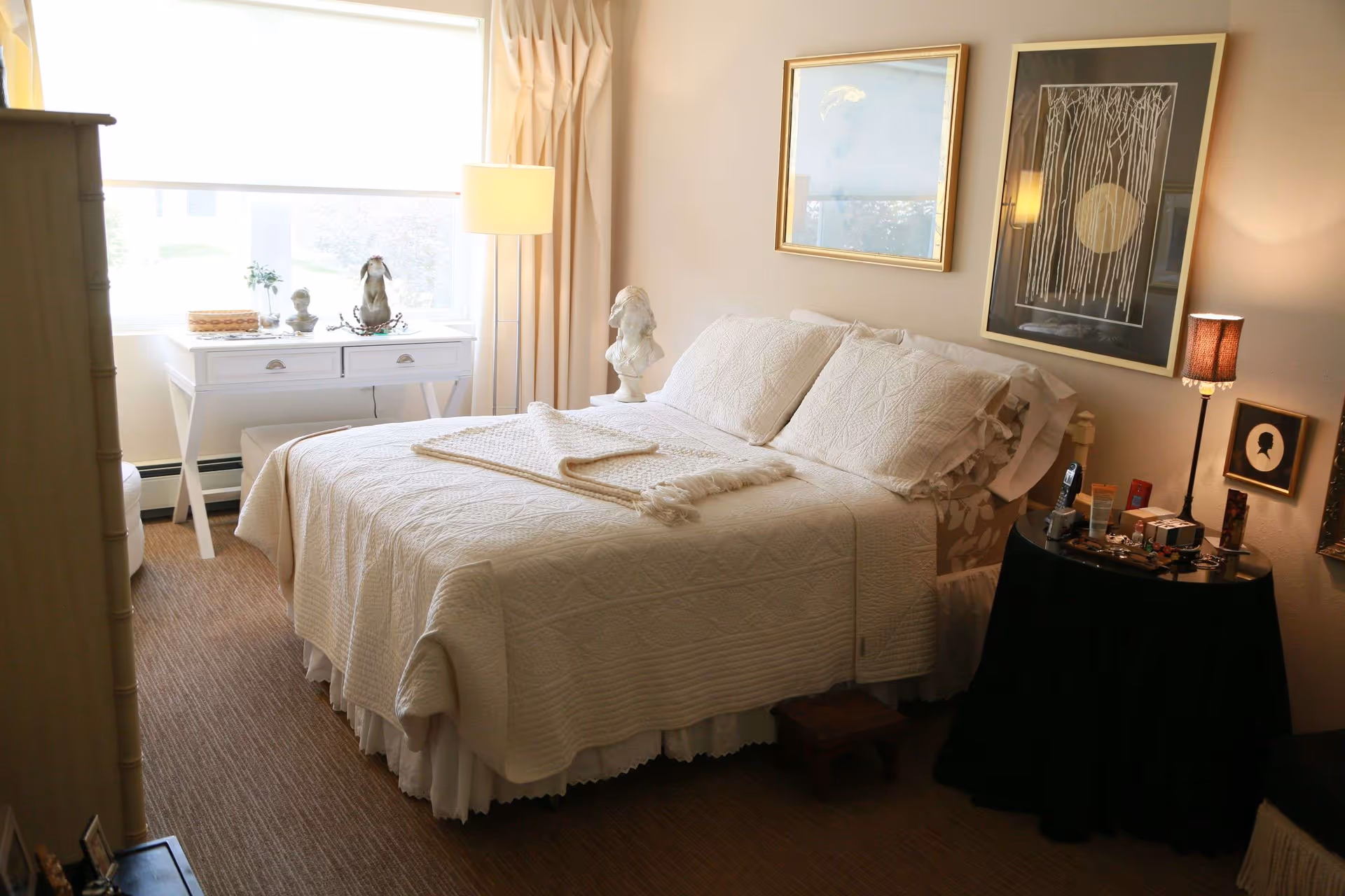 Bright, cozy bedroom with a neatly made bed, bedside table and lamp, and a desk by the window.
