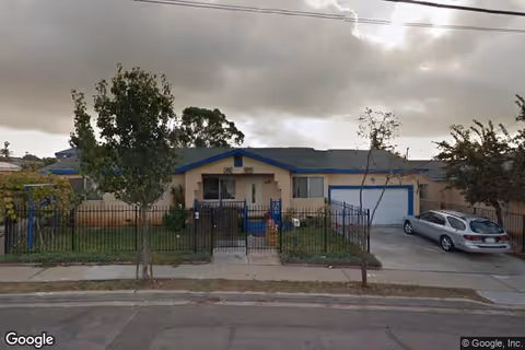 Single-story care home with blue trim, gated front yard, and a parked car.