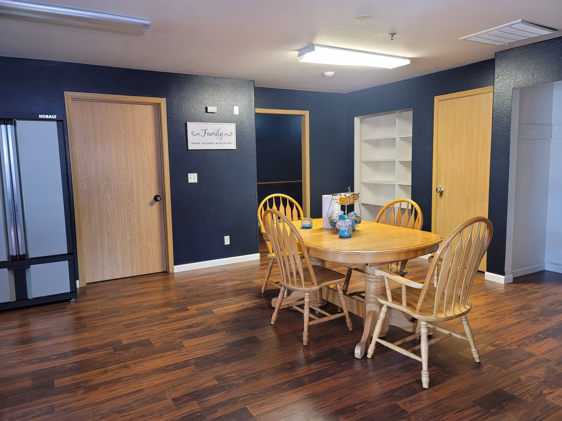 Wood dining table with six chairs in a blue-walled communal dining room.