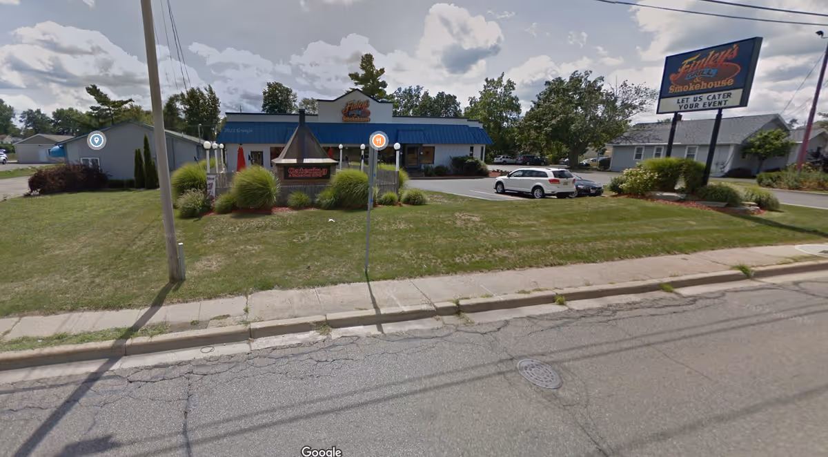 Exterior street view of a blue-roofed building with landscaped front and parked cars.