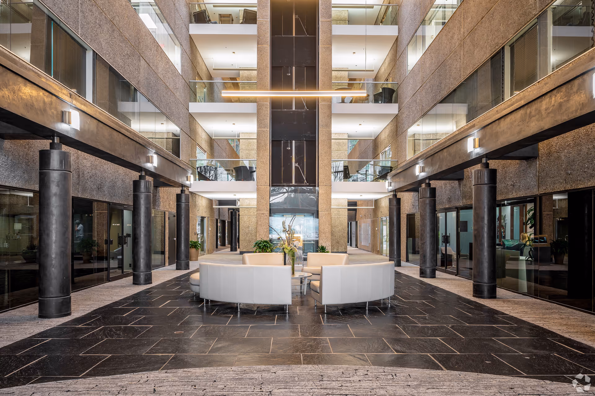 Modern interior lobby with black pillars, glass balconies, and circular cream seating.