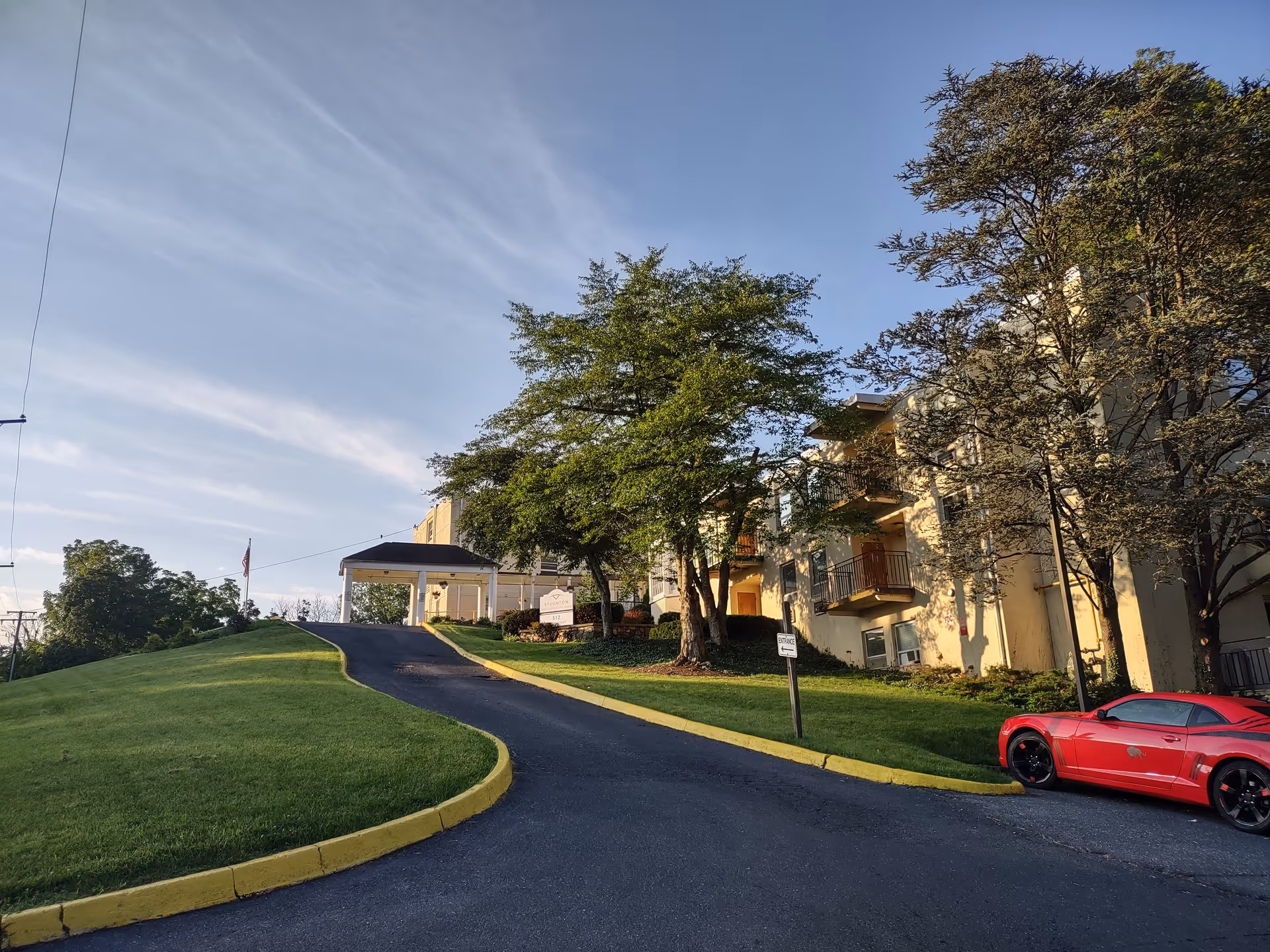 Exterior view of Envoy of Staunton with a curved driveway, trees, and a red car.