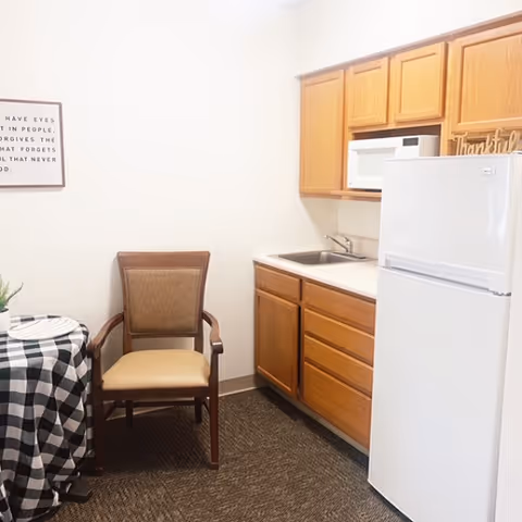Compact kitchen area with wooden cabinets, fridge, microwave, sink, and small dining table.