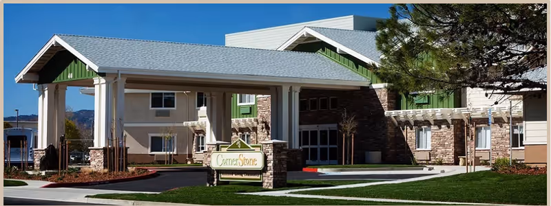 Exterior view of Cornerstone Assisted Living facility showing entrance, sign, and well-kept landscaping.