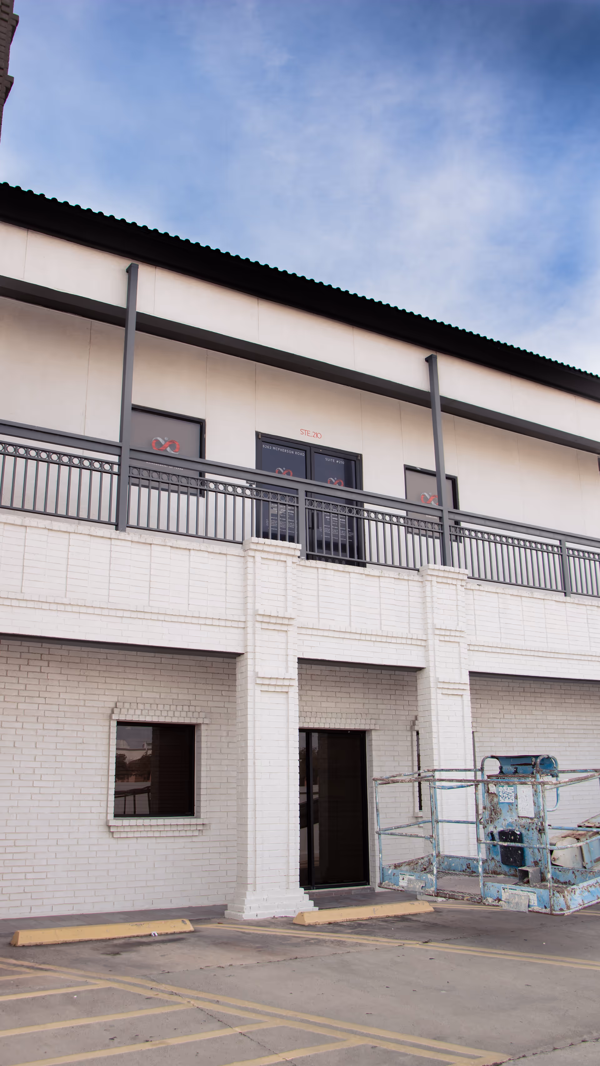 Two-story white brick facility exterior with balcony railings and a parked construction lift.