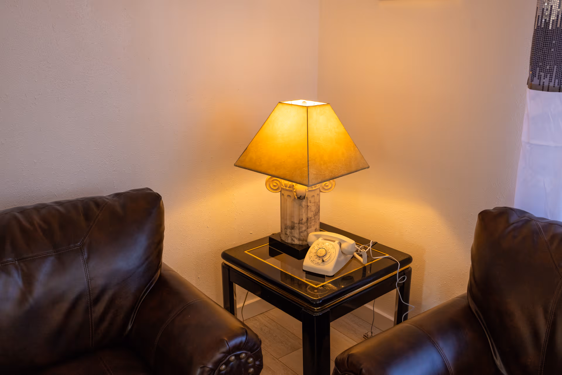 Two brown leather chairs flank a small table with lamp and telephone.