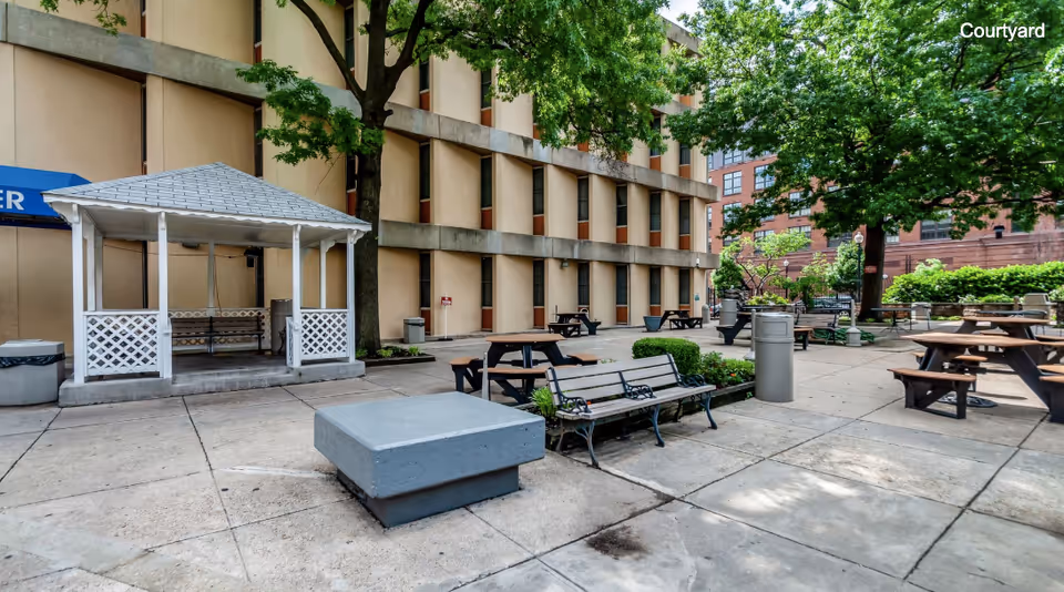 Courtyard with picnic tables, benches, a white gazebo, and a surrounding multi-story building.
