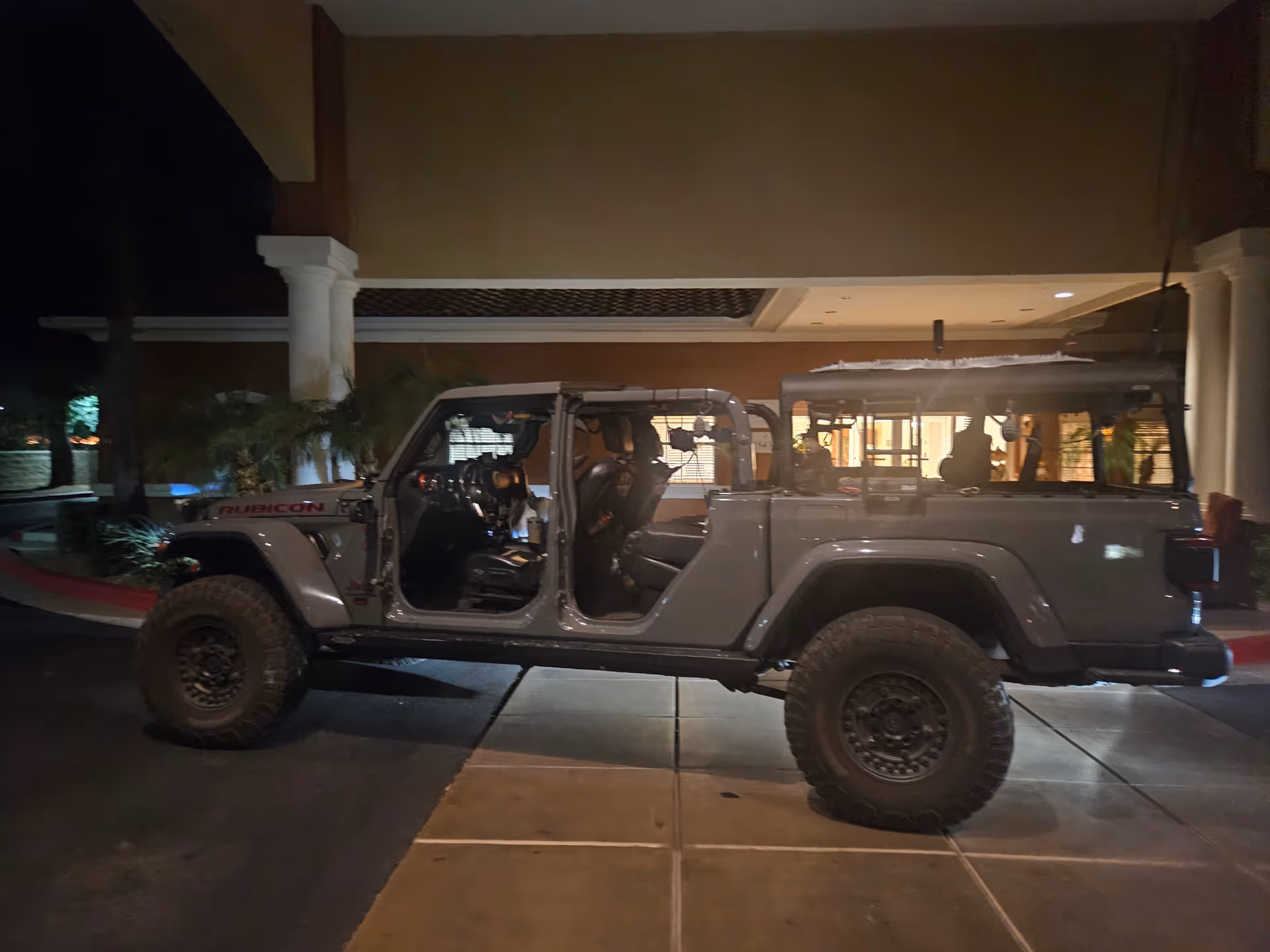 Gray Jeep Rubicon with open doors parked in front of a senior living facility at night.