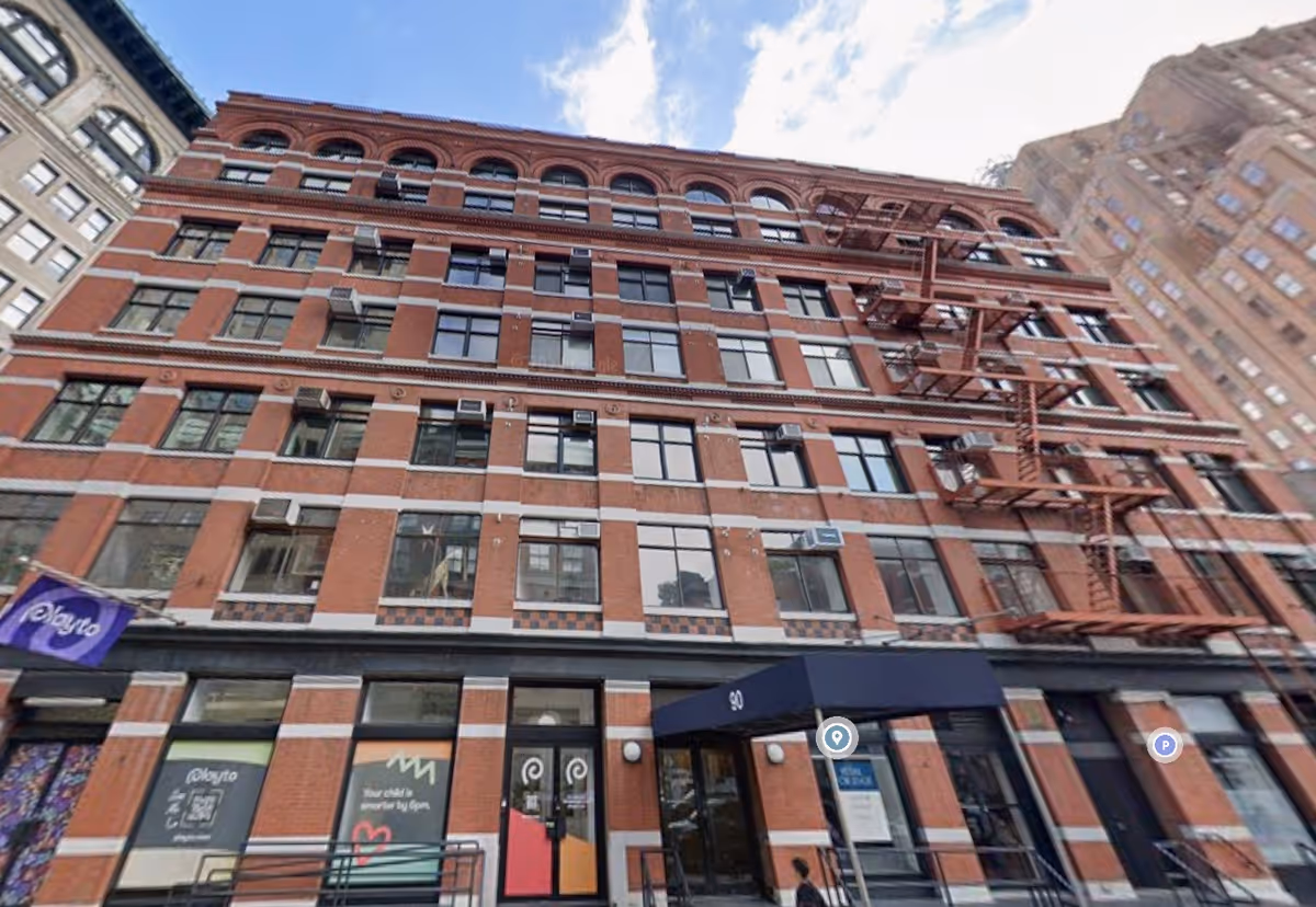 Red brick, multi-story building with fire escapes along a city street.