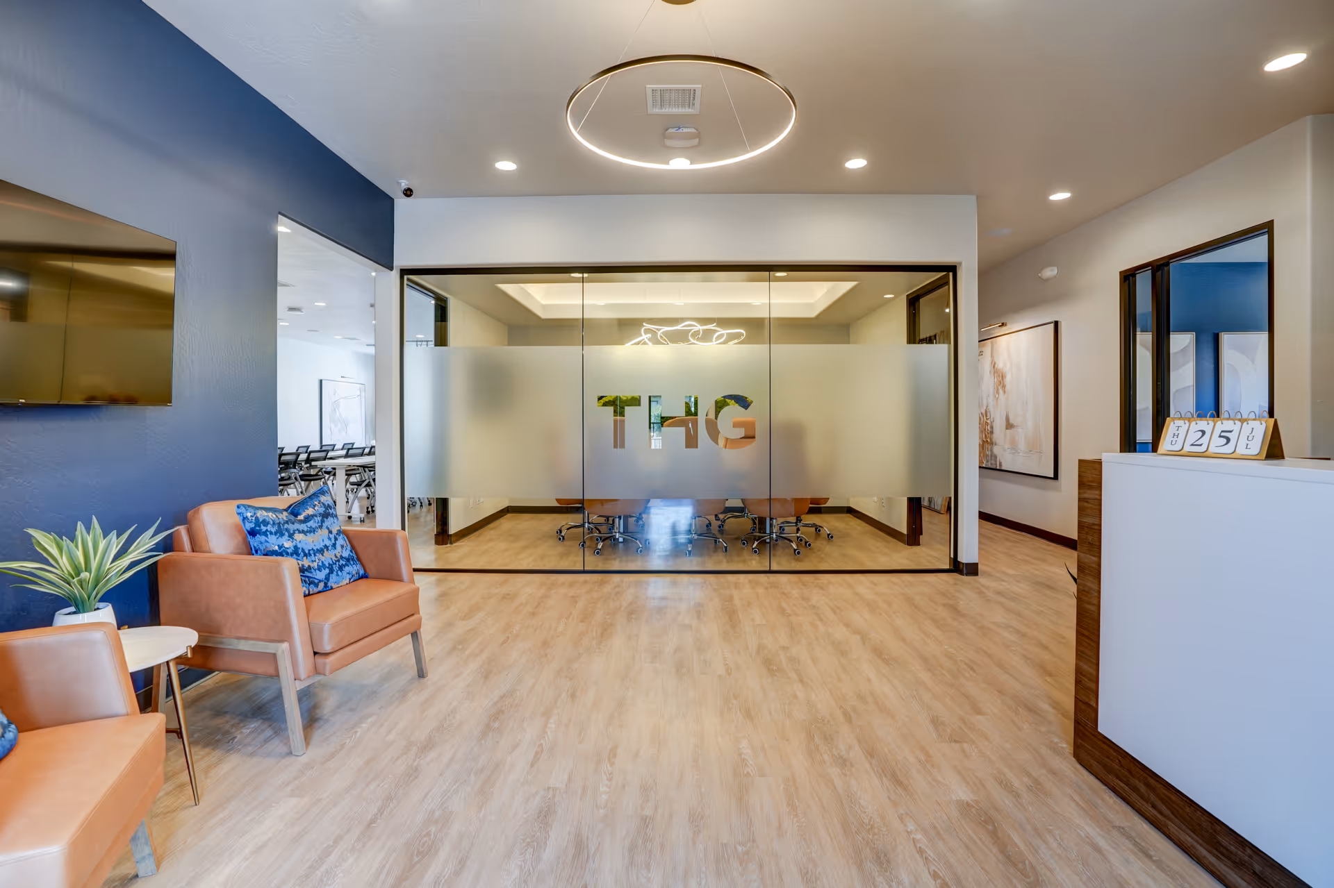Modern interior lobby with glass-walled conference room and orange lounge chairs.
