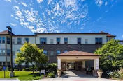 Exterior view of The Belcaro senior living facility with entrance, brick facade, and landscaping.