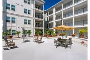 Outdoor courtyard of a senior living facility with tables, chairs, and a large umbrella.