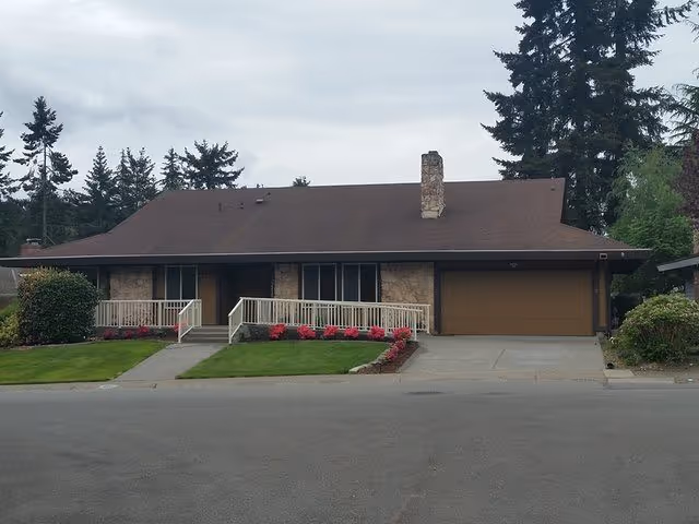 Front view of a single-story house with a brown roof, attached two-car garage, and landscaped lawn.