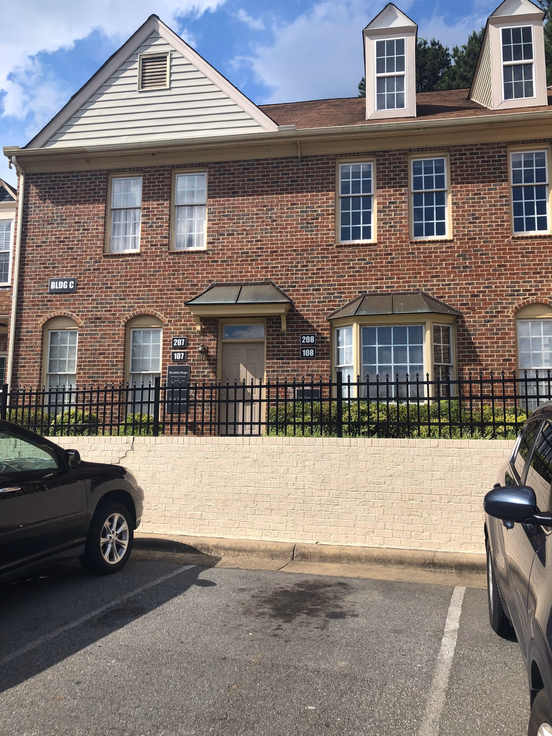 Brick multi-unit building facade with arched ground-floor windows, metal awnings, and a gated front.