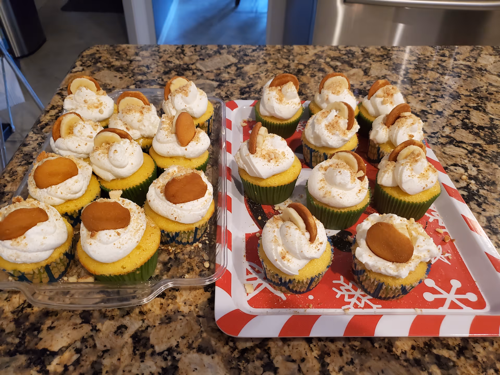 Trays of cupcakes with white frosting on a granite kitchen counter